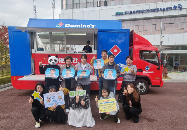 도미노피자 후원 파티카 앞에서 경기도시각장애인복지관 직원들이 도미노피자, 응원 피켓을 들고 기념 촬영을 하고 있다