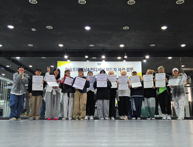 B2DTAINMENT가 운영하는 ‘머슬트레이닝&컨디셔닝 지도자 자격 검정’ 현장. 1기 교육생들이 교육 과정을 마치고 수료증을 수여받은 뒤 기념 촬영을 하고 있다. B2DTAINMENT는 2007년부터 토탈댄스지도자 자격 과정을 운영해왔으며, 2026년 머슬트레이닝&컨디셔닝 지도자 과정을 공식 론칭했다. 현장 중심 실습과 이론 교육을 병행하며 전문 지도자를 배출하고 있으며, 교육 수료 후 다양한 무대 및 현장 활동으로 연계되는 시스템을 구축하고 있다
