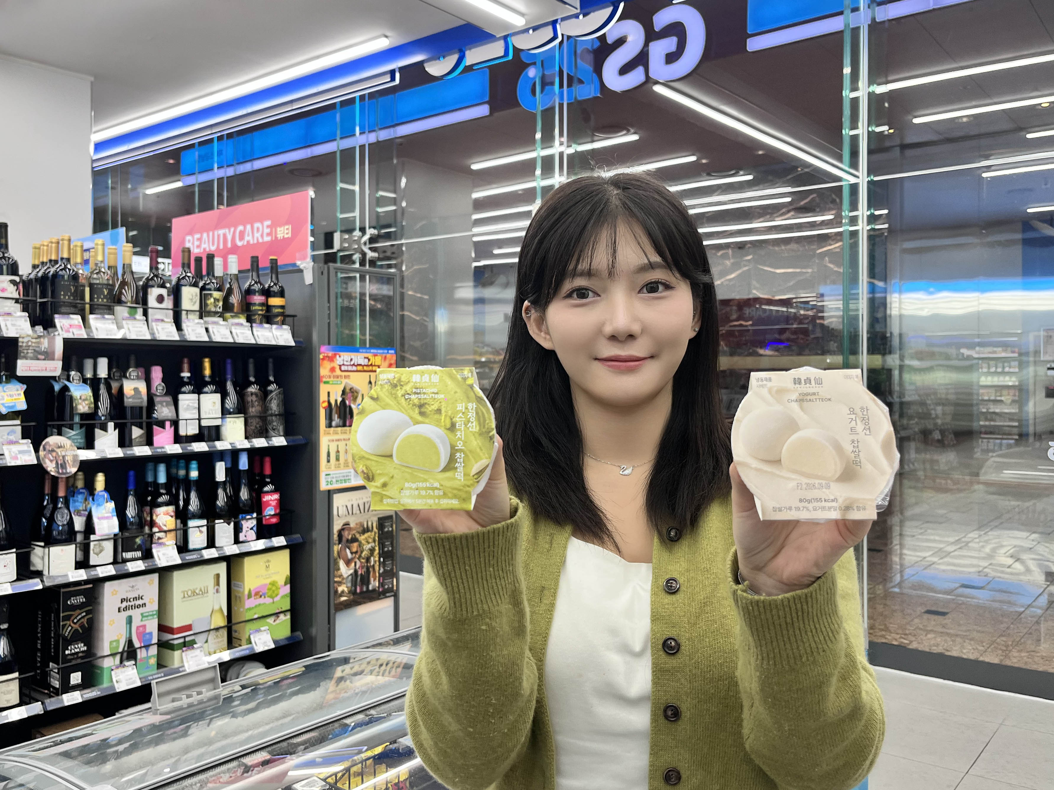 GS25 매장에서 모델이 초록색 피스타치오 찹쌀떡과 밝은색 요거트 찹쌀떡 포장을 들고 있다