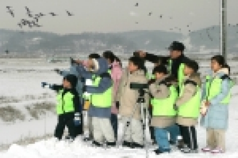 겨울철새들의 보금자리 민통선안 통일촌을 방문한 아동보호시설 아이들이 전봇대에서 미동도 않고 하늘의 제왕처럼 않아있는 독수리를 망원경으로 살펴보며 탄성을 지르고 있다. 주위로는 쇠기