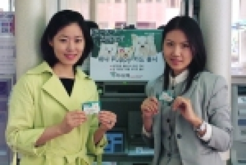 하나은행 직원 2명이 새로나온 '하나  Puppy카드'를 들고서  CD기 앞에서 활짝 웃고 있는 모습임 