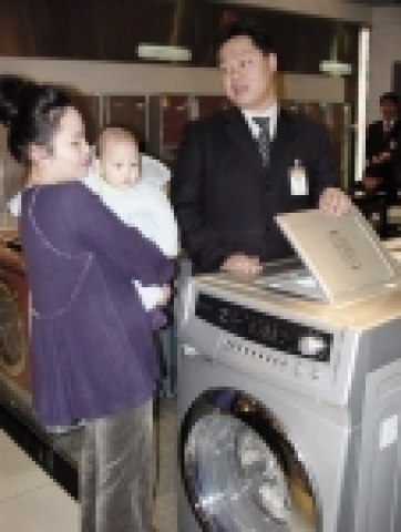 롯제백화점 가전담당 권병두 사원이 6개월된 아기 엄마에게 무세제 겸용 드럼세탁기 “클라쎄 멀티플러스”를 설명하고 있다.