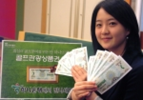 하나은행 직원이 은행 객장에서 골프관광상품권을 펼쳐 보이며 웃고 있는 모습임. 