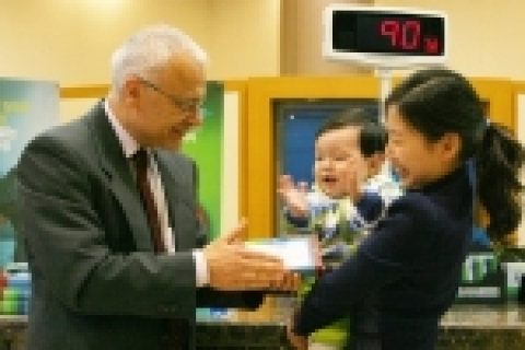SC제일은행 은행장(존 필메리디스)이 본점 영업부를 찾은 고객의 아기에게 통합1주년 기념 돌떡을 주는 장면