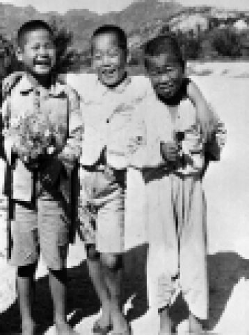 HQ47-0009/Photographer Unknown 1947년 한국. 서울 근교의 거리에서 세 명의 소년이 어깨동무를 한 모습으로 웃고 있다. 두 소년은 가슴에 꽃을 안고 있다. 2차 대전 종전 후 남한에 진주한 미군이 나누어준 초콜릿과 캔디는 한국 어린이들에게 큰 인기를 끌었다.