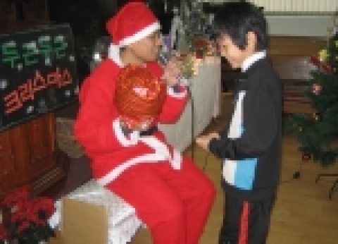 산타복을 입고 1일 산타가 된 형지어패럴 직원에게 크리스마스 선물을 받고 있는 큰사랑행복한홈스쿨 어린이