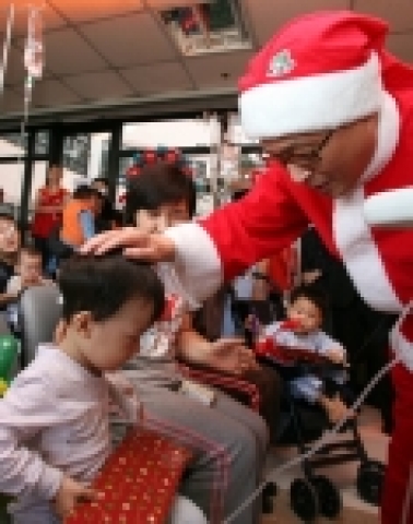 SK텔레콤 김신배 사장이 19일, 고려대 안암병원 소아병동을 방문하여, 산타클로스 복장으로 환아들을 격려하고 성탄선물을 나누어 주고 있다.