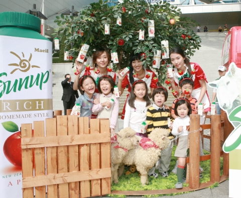 매일유업 썬업리치 애플 무료 시음행사에 참석한 어린이들이 사과 과수원 앞에서 양과 함께 포즈를 취하고 있다