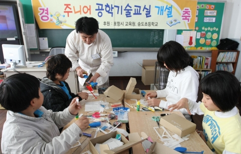 포항제철소 대기보전팀 이정엽 엔지니어(37세)가 '라이트형제 따라잡기' 수업을 지도하며, 송도초등학교 학생들과 함께 비행기를 만들고 있다.