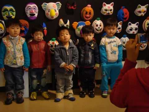어린이들이 자기가 만든 가면작품 앞에서 기념사진을 찍고 있다.
