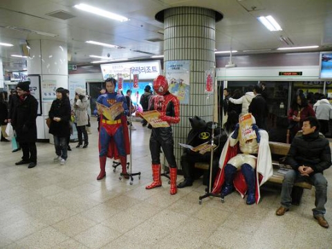 지하철 승강장에서 ‘슈퍼맨과 친구들’이 ‘2460’이라는 숫자가 새겨진 링거를 꽂고 퍼포먼스를 펼치고 있다.