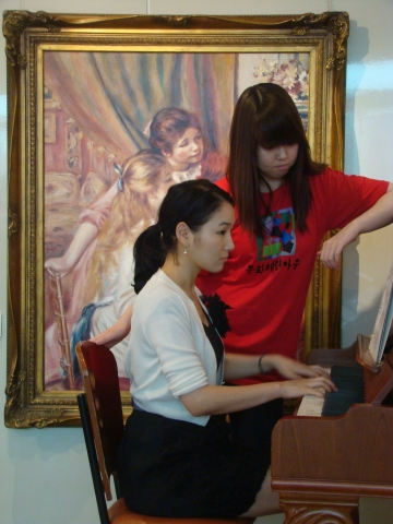 르느와르의&#039;피아노 치는 두 자매&#039;앞에서 실제로 똑 같은 포즈로 연주를 하고있다