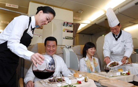 조리사 복장을 입은 아시아나 셰프 승무원(우측)과 소믈리에 복장을 갖춘 아시아나 소믈리에 승무원(좌측)이 각각 승객에게 요리와 와인을 서비스 하고 있다.