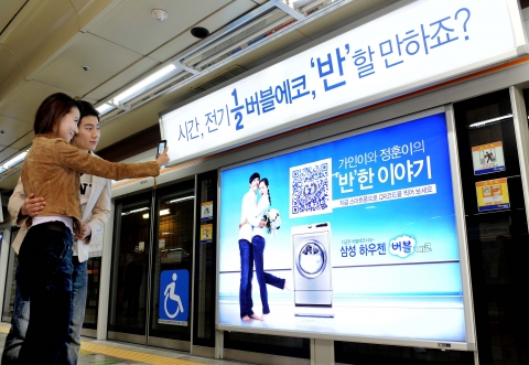 서울 교대역에서 젊은 남녀가 지하철 스크린도어의 삼성 하우젠 버블에코 QR코드 광고를 보고 직접 스마트폰으로 제품정보를 살펴보고 있다.