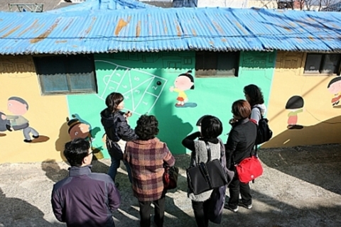 ‘신화마을’ 공공미술에 참여하고 있는 작가 김근숙씨가 현장을 방문한 에세이울산동인회 회원들에게 마을에 그려진 벽화를 설명하고 있다.