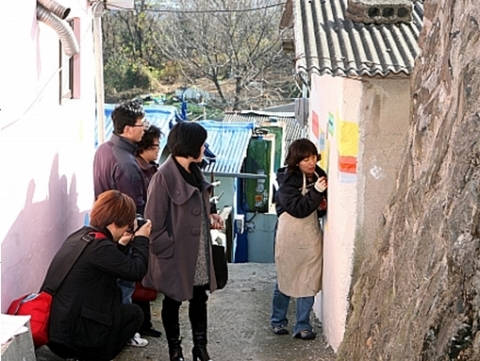 ‘신화마을’ 공공미술에 참여하고 있는 작가 김근숙씨가 현장을 방문한 에세이울산동인회 회원들에게 벽화작업과정에 대해 설명하고 있다.