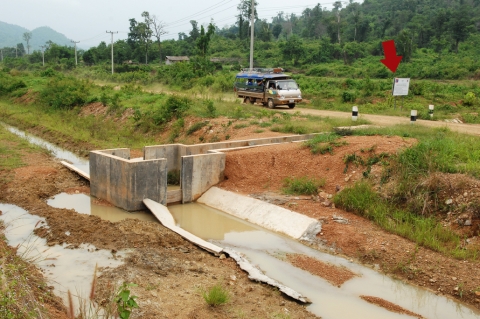 무너지고 부서진 문군 농업용관개수로 입구에 승객을 가득 태운 문군 마을버스가 질주하고 있다. 바로 옆에 입간판과 대각선으로 뼈대가 드러난 부서진 분수공이 보인다. 화살표 부분이 태
