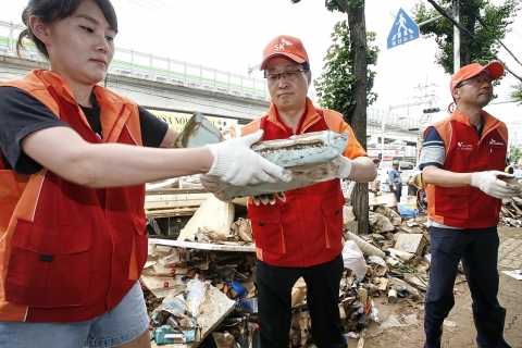 김신배 SK자원봉사단장(SK그룹 부회장, 사진 가운데)이 지난 30일 경기도 동두천시 수해지역에서 윤진원 SK(주) 윤리경영부문장(사진 오른쪽) 등 임직원들과 함께  복구작업을 돕