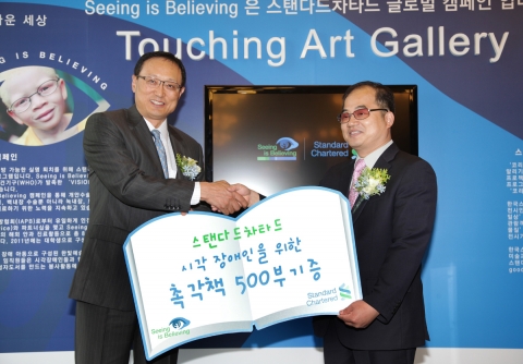 한국스탠다드차타드금융지주는 10일 오전, 서울 중구 충무로 소재 스탠다드차타드제일은행(SC제일은행) 제일지점에서 세계 시력의 날(10월 13일)을 기념하여 시각장애인을 위한 ‘터칭 아트 갤러리(Touching Art Gallery)’ 개관식을 가졌다. ‘Seeing is Believing 캠페인’ 한국 의장인 SC제일은행 안정모 부행장(사진 왼쪽)이 시각장애인협회 최동익 회장에게 촉각책을 기증하고 있다.