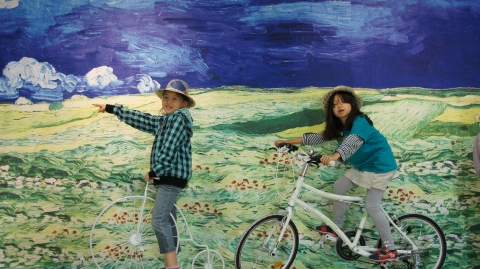 이번 전시중 가장 인기가 많은 고흐의&#039;폭풍아래 밀밭&#039;에서 어린이들이 자전거를 타고 밀밭을 달리는 모습으로 사진을 찍고있다