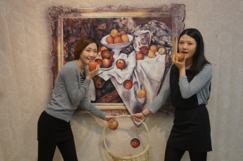 세잔의&#039;사과와 오렌지&#039;패러디 작품앞에서 실제 사과를 들고 떨어지는 사과를 바구니에 담는 장면을 연출하며 즐거워하고 있다