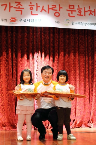 2012 한사랑 문화체험에서 우정사업본부 이현철 보험사업단장(가운데)이 함께 참여한 소아암 어린이 홍보대사 김보미(왼쪽), 이예나(오른쪽) 어린이에게 대표로 기념선물을 전달하고 있다. (사진제공=한국백혈병어린이재단)