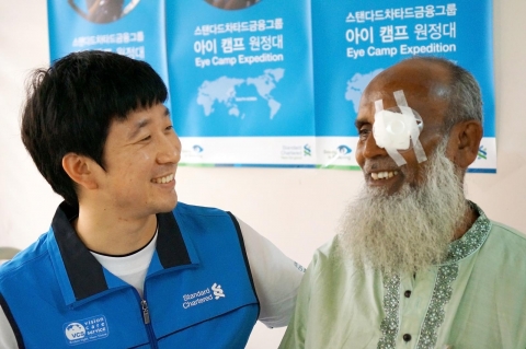 한국스탠다드차타드금융그룹의 해외안과의료봉사단인 ‘아이캠프(Eye Camp)원정대’와 국제실명구호단체인 비전케어가 방글라데시 사바 지역에서 개안수술 및 안과진료 봉사활동을 실시했다. 한국스탠다드차타드은행 직원 봉사자와 방글라데시 환자가 환하게 웃고 있다. ‘아이캠프원정대’는 예방가능한 실명퇴치를 위해 스탠다드차타드가 진행하고 있는 Seeing is Believing 캠페인 일환인 지속가능경영활동이다.