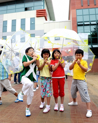 투명우산을 전달받은 아이들이 우산에 달린 호루라기를 불며 포즈를 취하고 있다.
