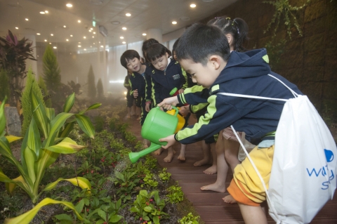 워터스토리를 방문한 청심 홉스쿨 어린이들이 1층 실내정원에서 화초에 물을 주는 체험행사를 갖고 있다. 이곳은 벽면과 바닥에서 이끼와 식물들이 자라는 공간으로서 수증기와 어울려 몽환적이고 색다른 경험을 제공한다.