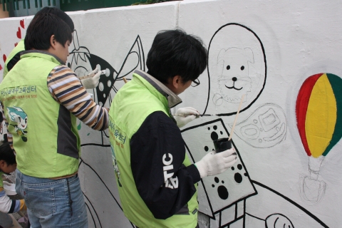 부산사회복무교육센터 벽화봉사동아리가 지역 주민들을 위해 허름한 벽면에 그림을 그리고 있다.