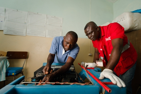 코카콜라의 선임 냉각기술자 맥스웰 아이시(Maxwell Ayisi, 오른쪽)과  가나(Ghana) 보건 서비스 냉장 기술자 리빙스톤 모데이(Livingstone Modey, 왼쪽)이 가나의 볼타 지역 페키 드자케(Peki Dzake)의 한 병원에서 백신 보관용 가스/전기 겸용 냉각기를 수리하고 있다.