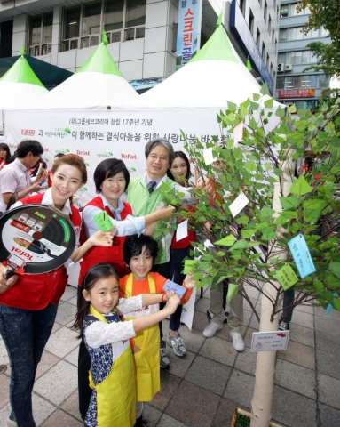 9월 18일 무교동 어린이재단 본부 앞 광장에서 진행된 테팔, 사랑나눔 바자회에서 팽경인 테팔 대표 및 직원들과 이충로 초록우산 어린이 재단 본부장이 결식아동들을 위한 응원의 메시지를 희망트리에 달고 있다.