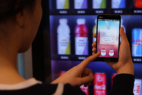 사용자가 스마트벤딩머신 앞에서 앱으로 자판기 기능을 구동하는 모습이다.