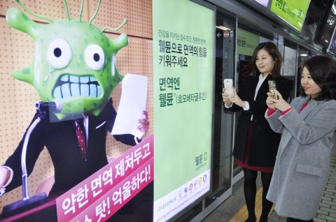 서울 강남역 지하철 승강장에서 지하철을 기다리는 사람들이 내츄럴엔도텍 웰뮨 광고 인증샷 이벤트에 참여하기 위해 광고 사진을 찍는 모습.