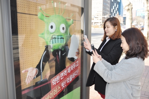 서울 신논현역 버스 정류장에서 버스를 기다리는 사람들이 내츄럴엔도텍 웰뮨 광고 인증샷 이벤트에 참여하기 위해 광고 사진을 찍는 모습.