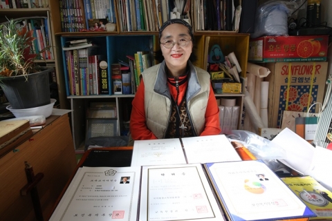 송영희 씨가 검정고시 합격증명서와 사회복지학 학위, 사회복지사 2급 및 보육교사 2급 자격증을 보여주며 환하게 웃고 있다.