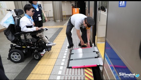 일본 역무원의 안내를 받아 전동휠체어로 전철을 이용하고 있다