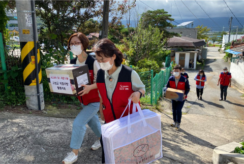 NCMN 봉사자들이 이브자리 이불, 한과 세트, 생필품을 담은 사랑 나눔 박스를 들고 고성군 담당자와 함께 독거노인 가정을 방문하고 있다