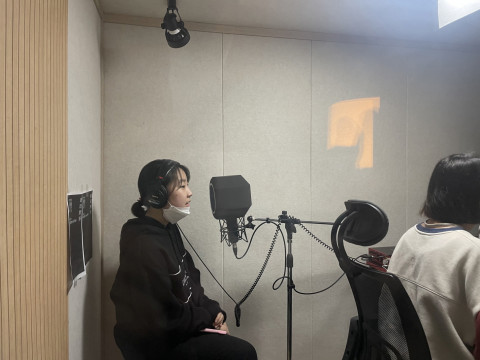 참가자들이 녹음 스튜디오에서 노래 파트 녹음을 작업하고 있다