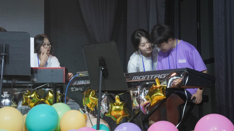 대학생 교사의 따뜻한 눈맞춤과 손길 속에서 한 참가 아동이 건반 위에 손을 얹고 있다