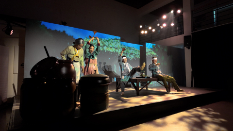 뮤지컬에서 1920년대 삼례의 한 마을, 주인공인 복실(주걱을 들고 있는 소녀)과 할매, 그리고 마을 주민들이 막걸리를 마시며 노래를 부르는 모습