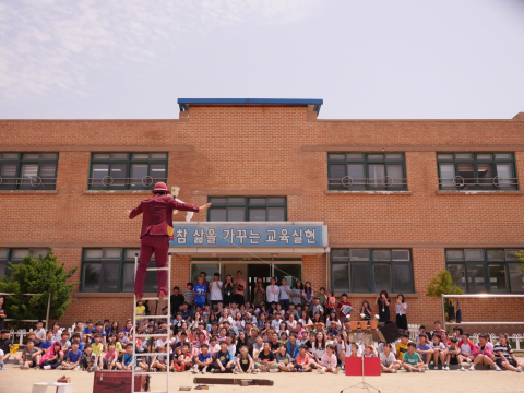 학교 운동장에서 자연과 함께 서커스 공연을 관람하는 아이들