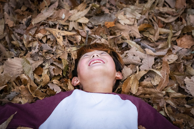 글꽃숲 참가 아동이 낙엽 가득한 숲에 누워 행복하게 웃고 있다