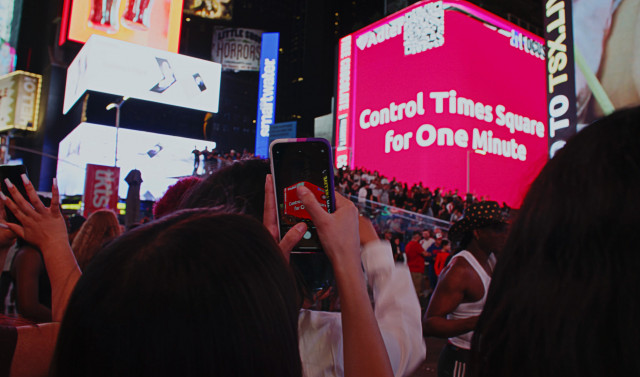 뉴욕 타임스퀘어의 행인들이 아들러 광고를 기다리며 QR코드를 스캔하고 있다