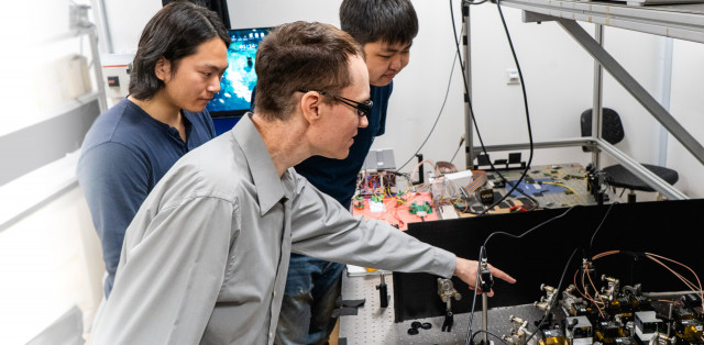 Associate Professor Aaron Danner, center, with PhD students Zifeng Yuan, left, and Yuan Gao, right, all from the NUS Department of Electrical and Computer Engineering, at an all-optical Ising machine that was designed and built by Gao. (Photo: Business Wire)