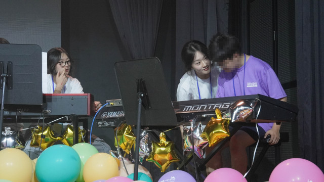 대학생 교사의 따뜻한 눈맞춤과 손길 속에서 한 참가 아동이 건반 위에 손을 얹고 있다