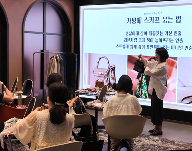 배선영이 스카프를 가방 손잡이와 스트랩 등에 활용해 기존 가방에 새로운 분위기를 더하는 실전 스타일링 방법을 직접 시연하고 있다