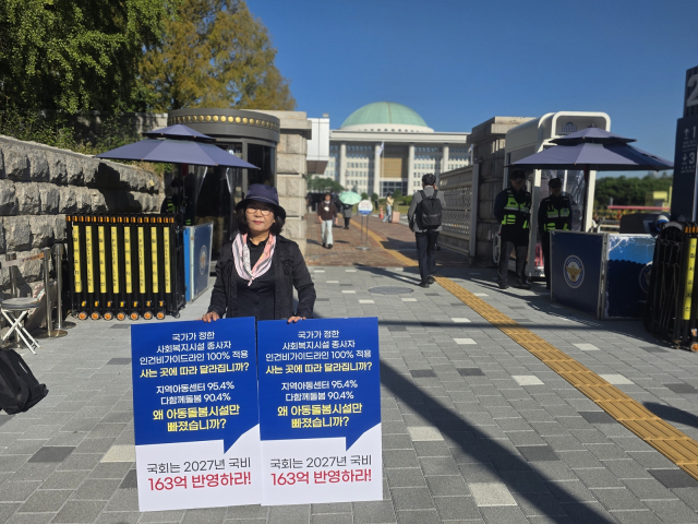 국정감사가 진행 중인 국회 정문 앞에서 한 지역아동센터 관계자가 인건비 가이드라인 100% 적용을 촉구하는 피켓을 들고 1인 시위를 벌이고 있다
